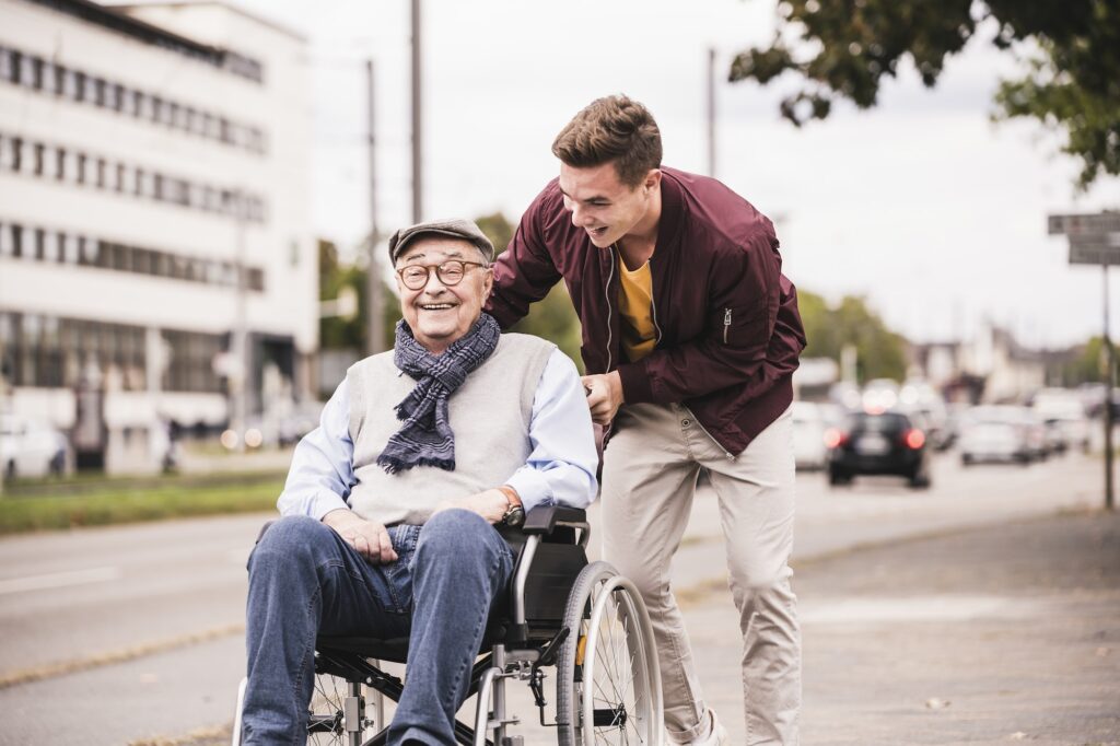 Young man pushing happy senior man in wheelchair